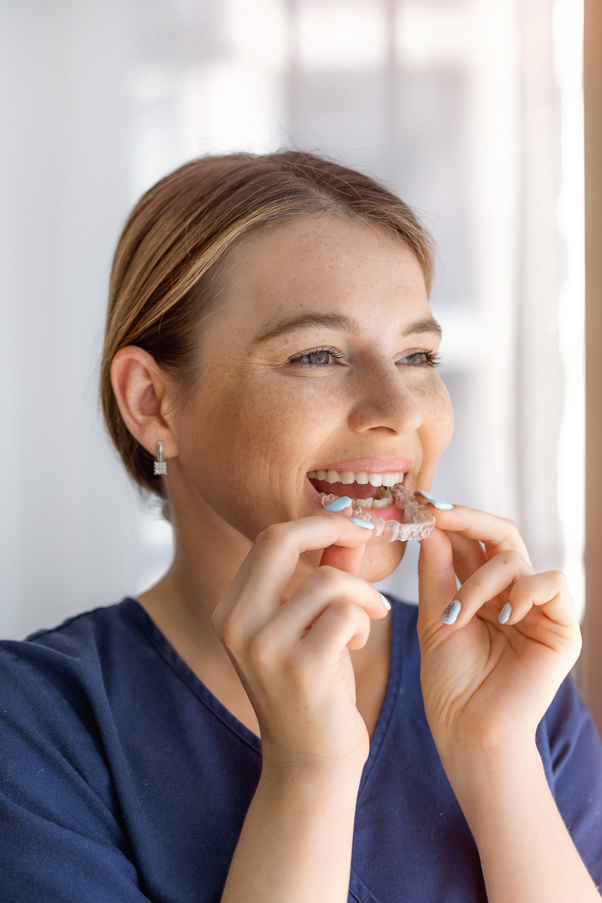 A cheerful woman gently places a clear aligner for correcting orthodontic teeth visibility issues